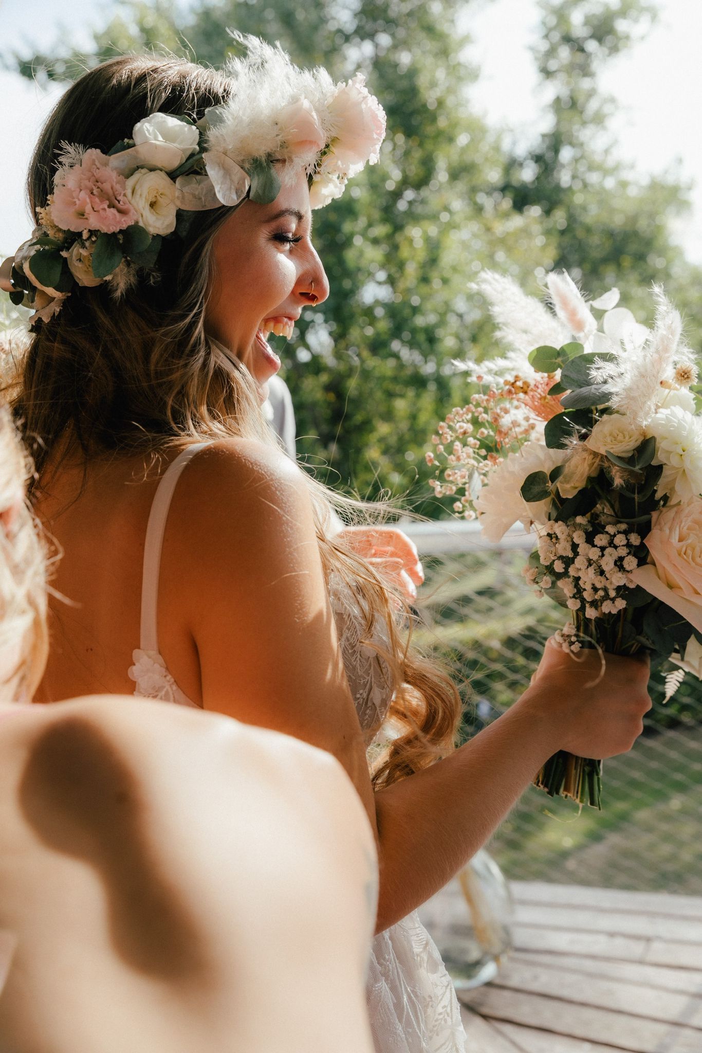 Die Braut trägt einen Blumenkranz und hält einen Blumenstrauß in der Hand.