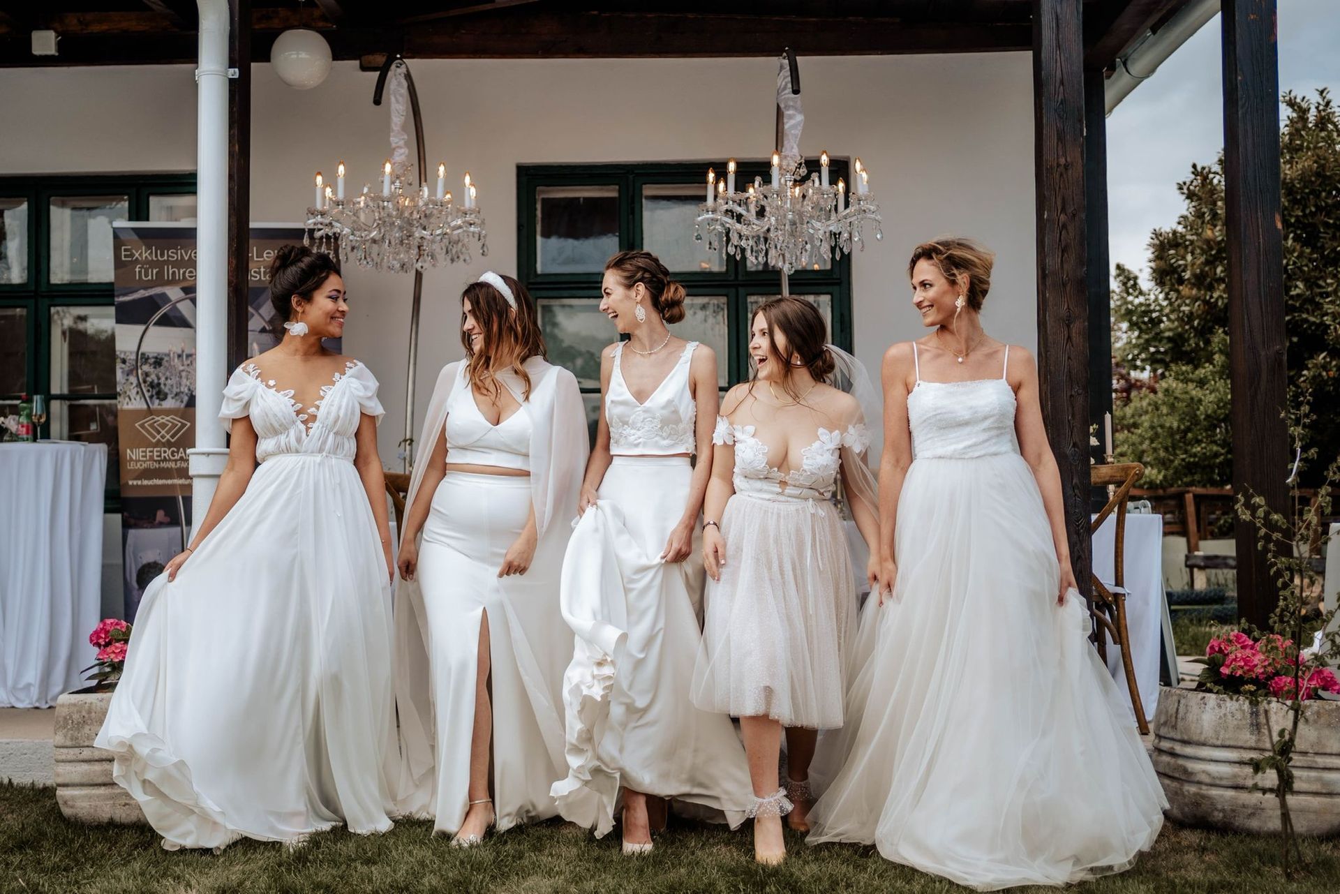 Eine Gruppe von Frauen in Brautkleidern steht nebeneinander vor einem Gebäude.