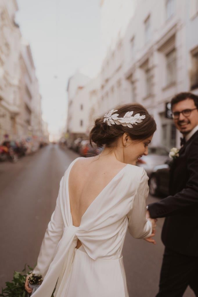 Eine Braut und ein Bräutigam gehen die Straße entlang. Die Braut trägt ein weißes Kleid mit einer Schleife auf dem Rücken.