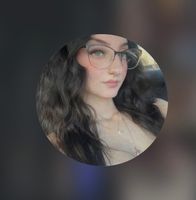 Woman with long brown hair wearing glasses, smiling, and looking at the camera.