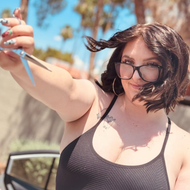 Woman with dark hair smiles, wearing a gray plaid blazer and white shirt, tan background.