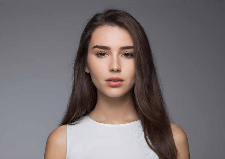Woman with long brown hair, wearing a white sleeveless top, looking directly at the camera.
