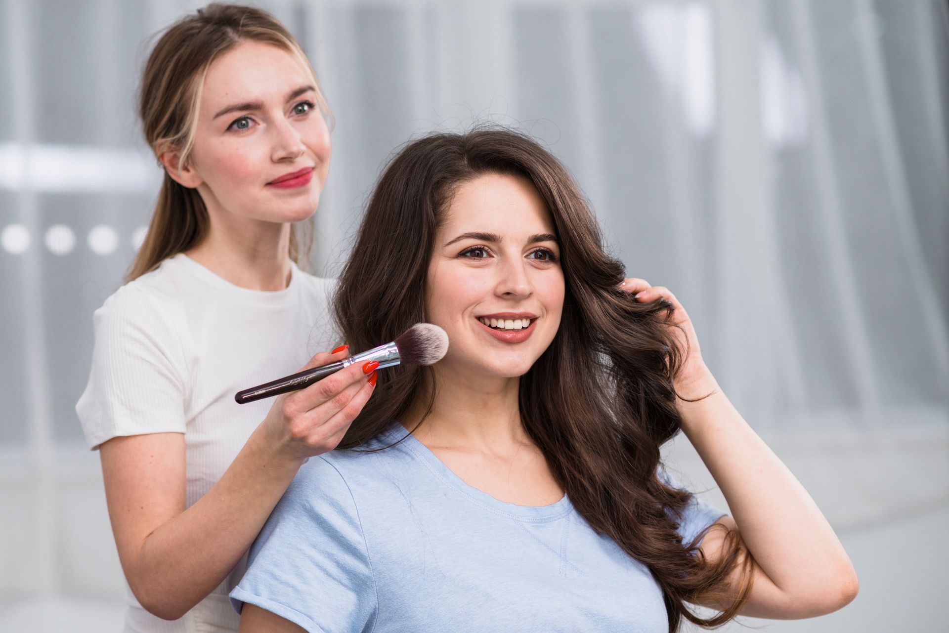 Woman getting makeup applied by another woman with a makeup brush.