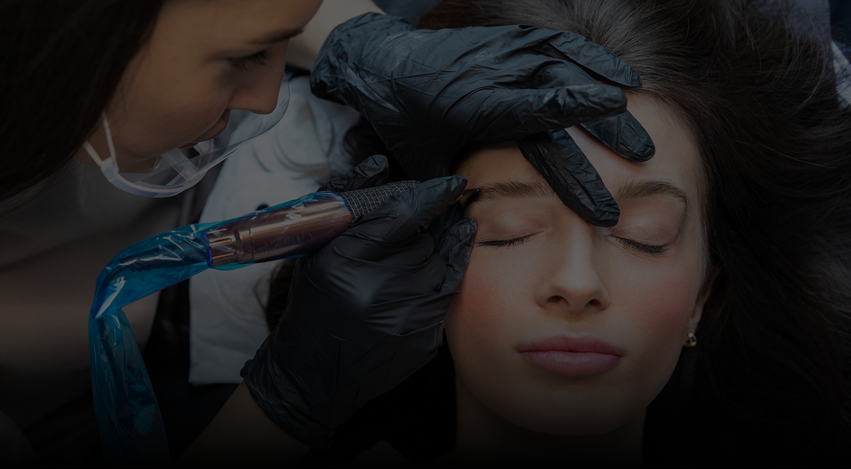 Woman receiving eyebrow microblading procedure. Person in gloves using tattoo pen.