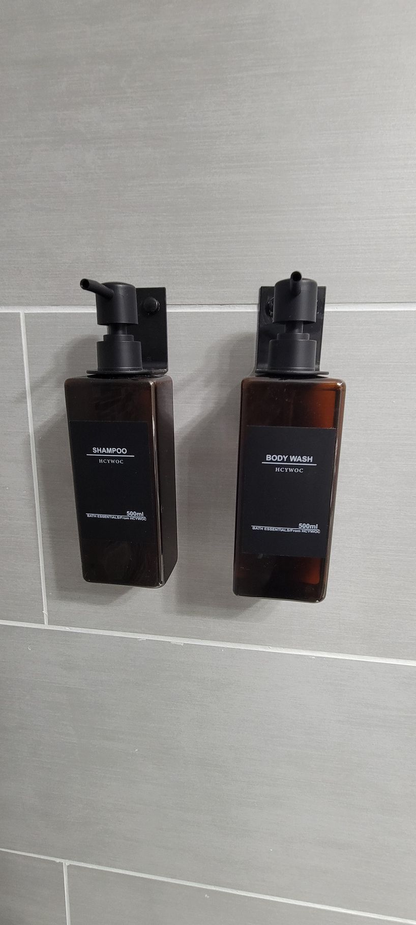 Two bottles of soap are hanging on a tiled wall.