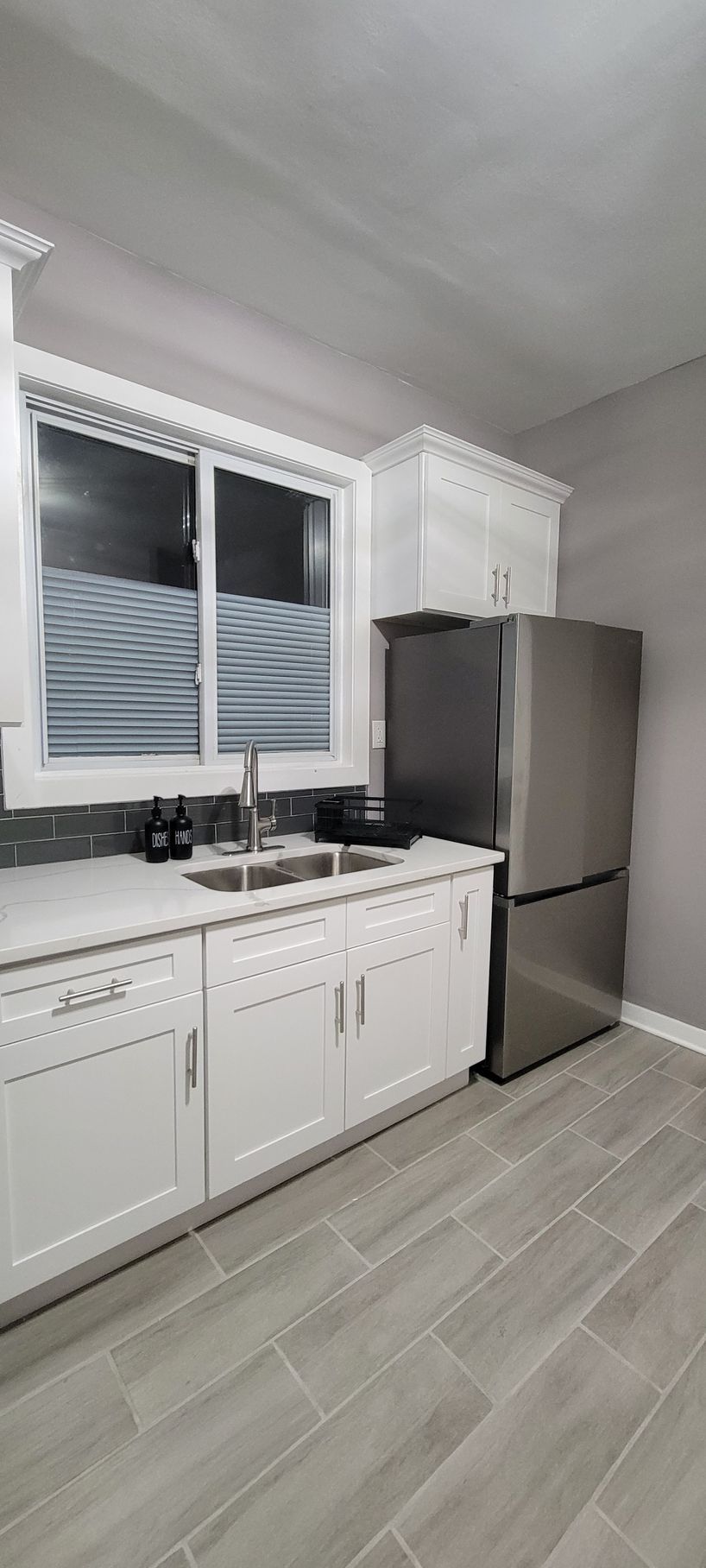 A kitchen with white cabinets , a stainless steel refrigerator , a sink , and a window.