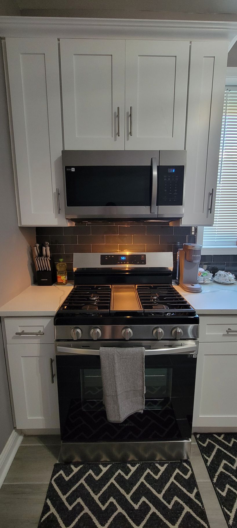 A kitchen with a stove , oven , microwave and white cabinets.