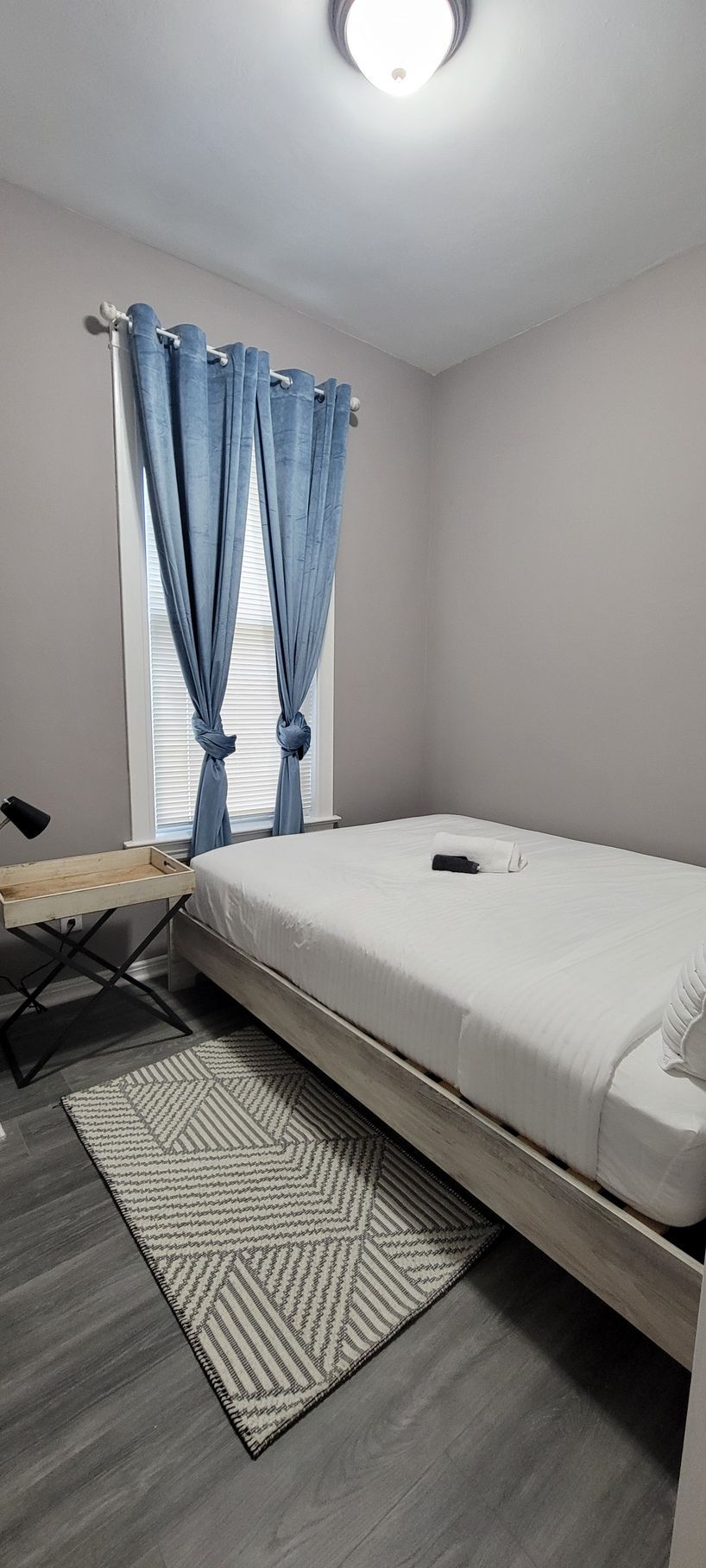 A bedroom with a bed , rug , window and curtains.