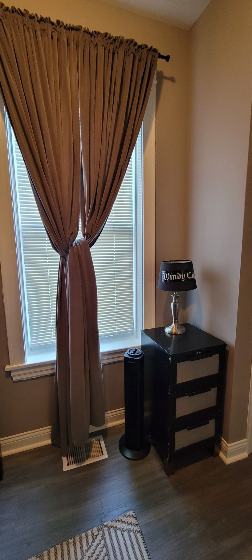 A bedroom with a window , nightstand , lamp and curtains.