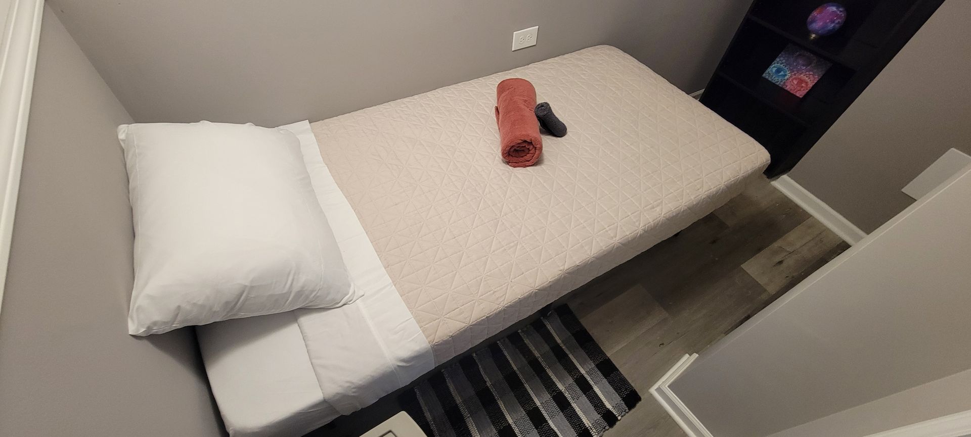 A single bed with a pillow and a towel on it in a small room.