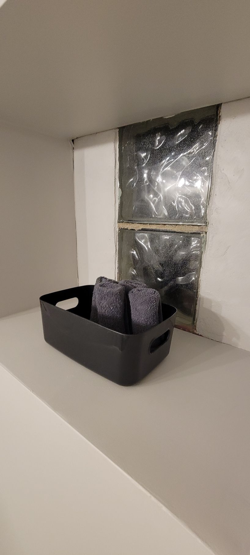 A black tray filled with towels is sitting on a shelf next to a window.