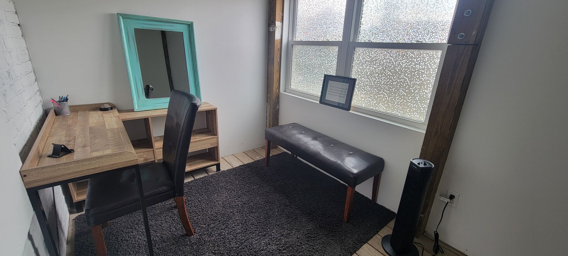 A room with a desk , chair , bench , mirror and window.