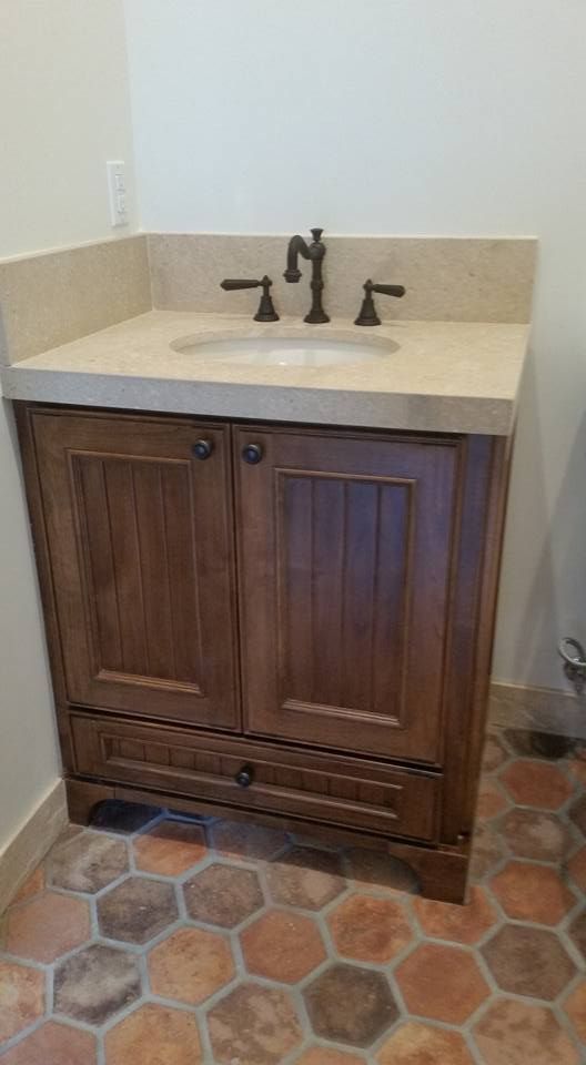A bathroom vanity with a sink and faucet on a tiled floor.