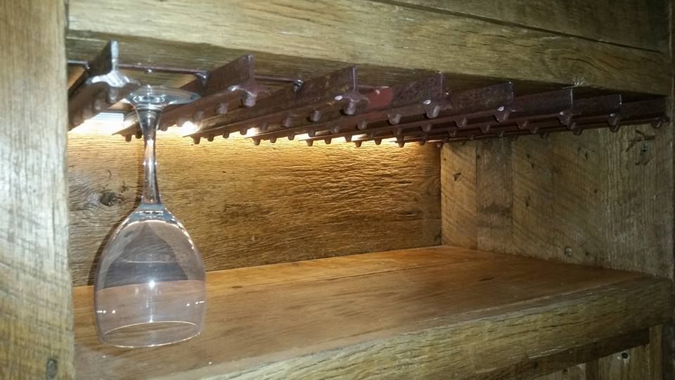 A wine glass is hanging from a wine rack on a wooden shelf.