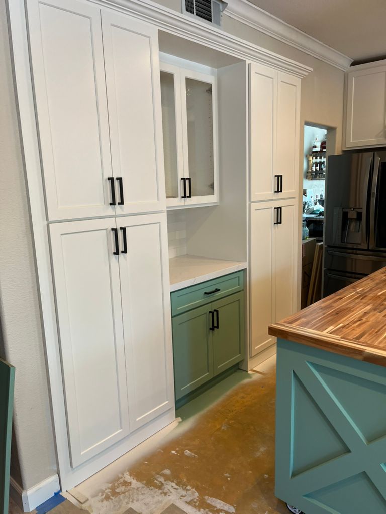 A kitchen with white cabinets and green cabinets and a blue island.