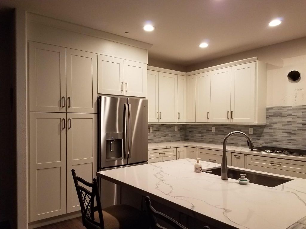 A kitchen with white cabinets , stainless steel appliances , a sink and a refrigerator.