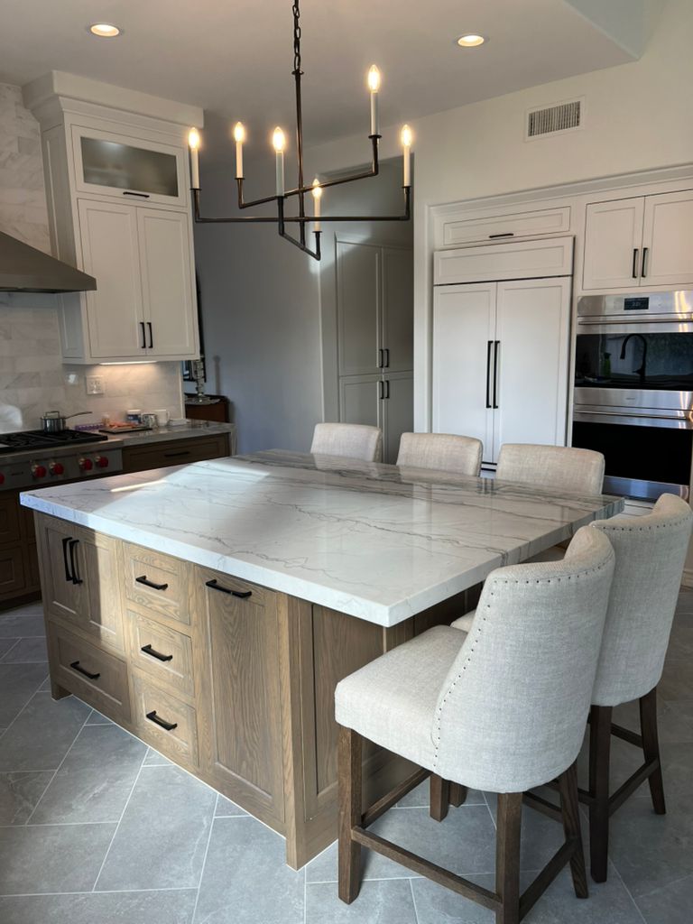 A kitchen with a large island and chairs and a chandelier hanging from the ceiling.