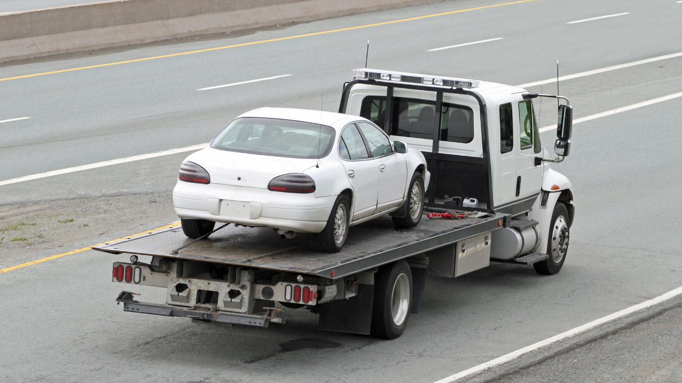 A white car is being towed by a tow truck on a highway.