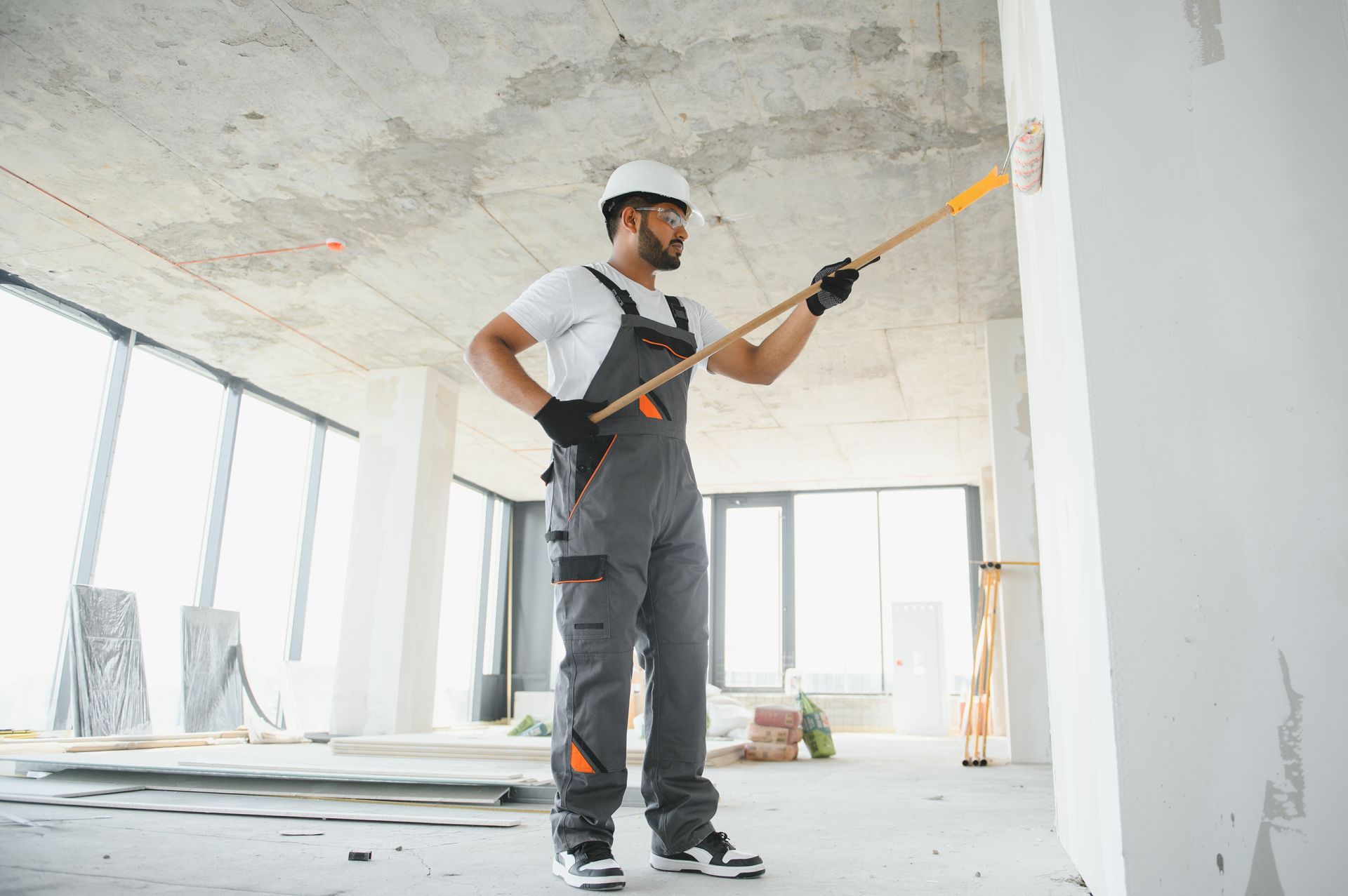 Construction worker in safety gear using a tool on a white wall. Interior construction site.