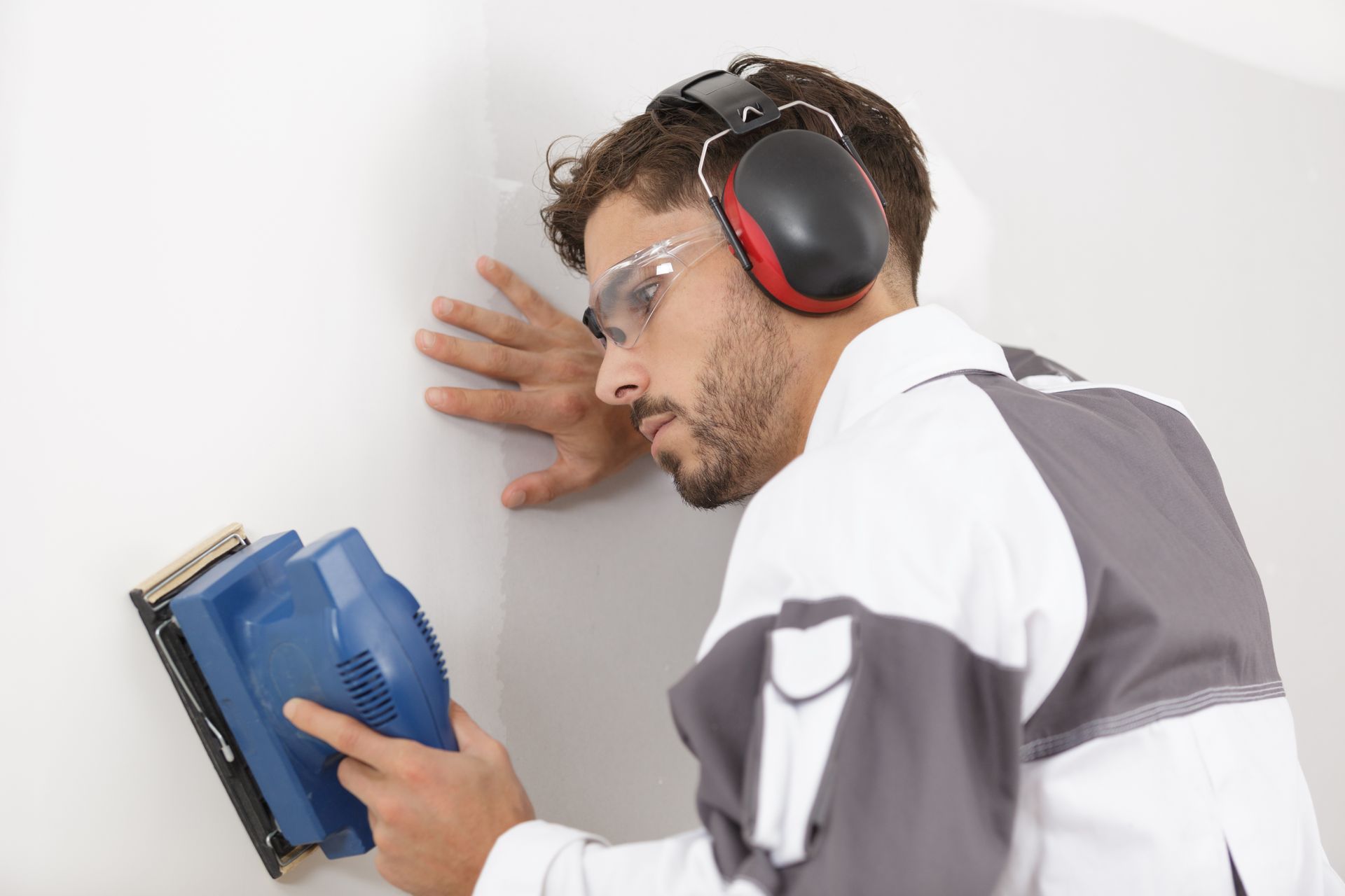 Man sanding drywall, wearing safety glasses and earmuffs.