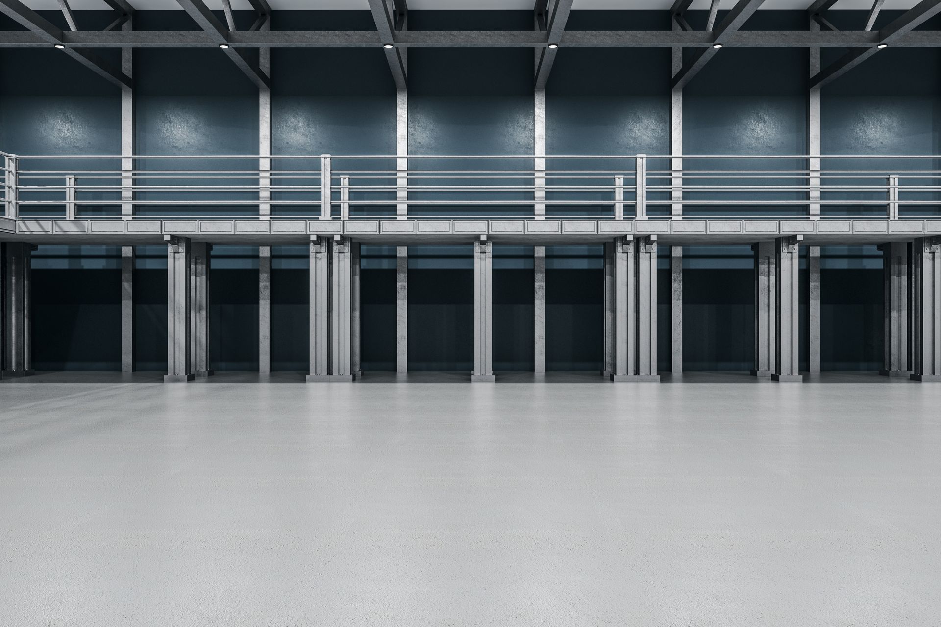 Large empty warehouse with a gray concrete floor, metal support beams, and a second-level platform.