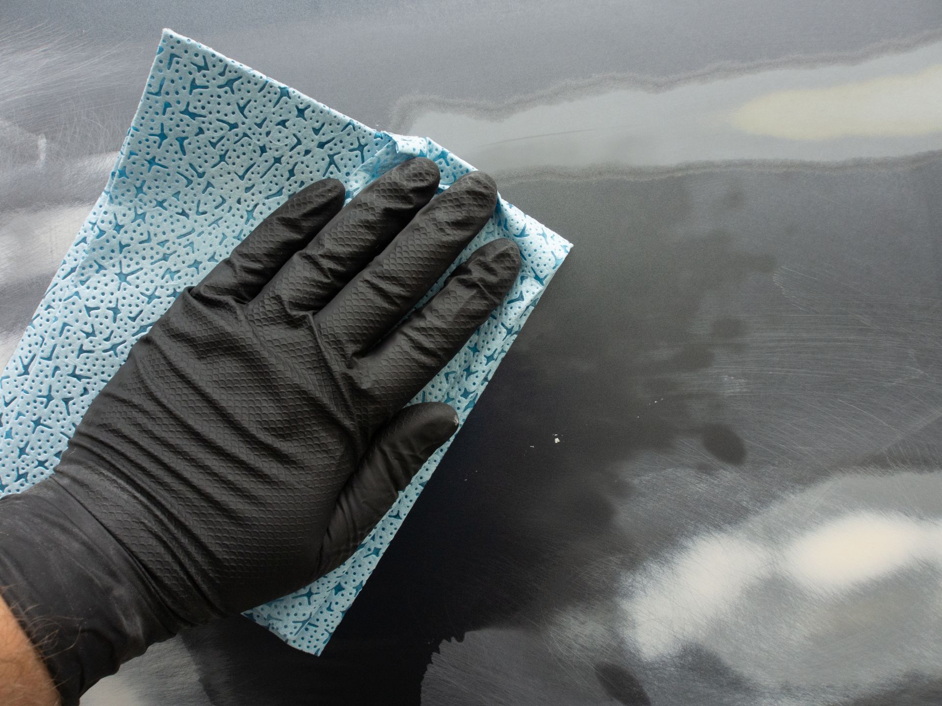 Gloved hand wiping a dark surface with a blue and white patterned cloth.