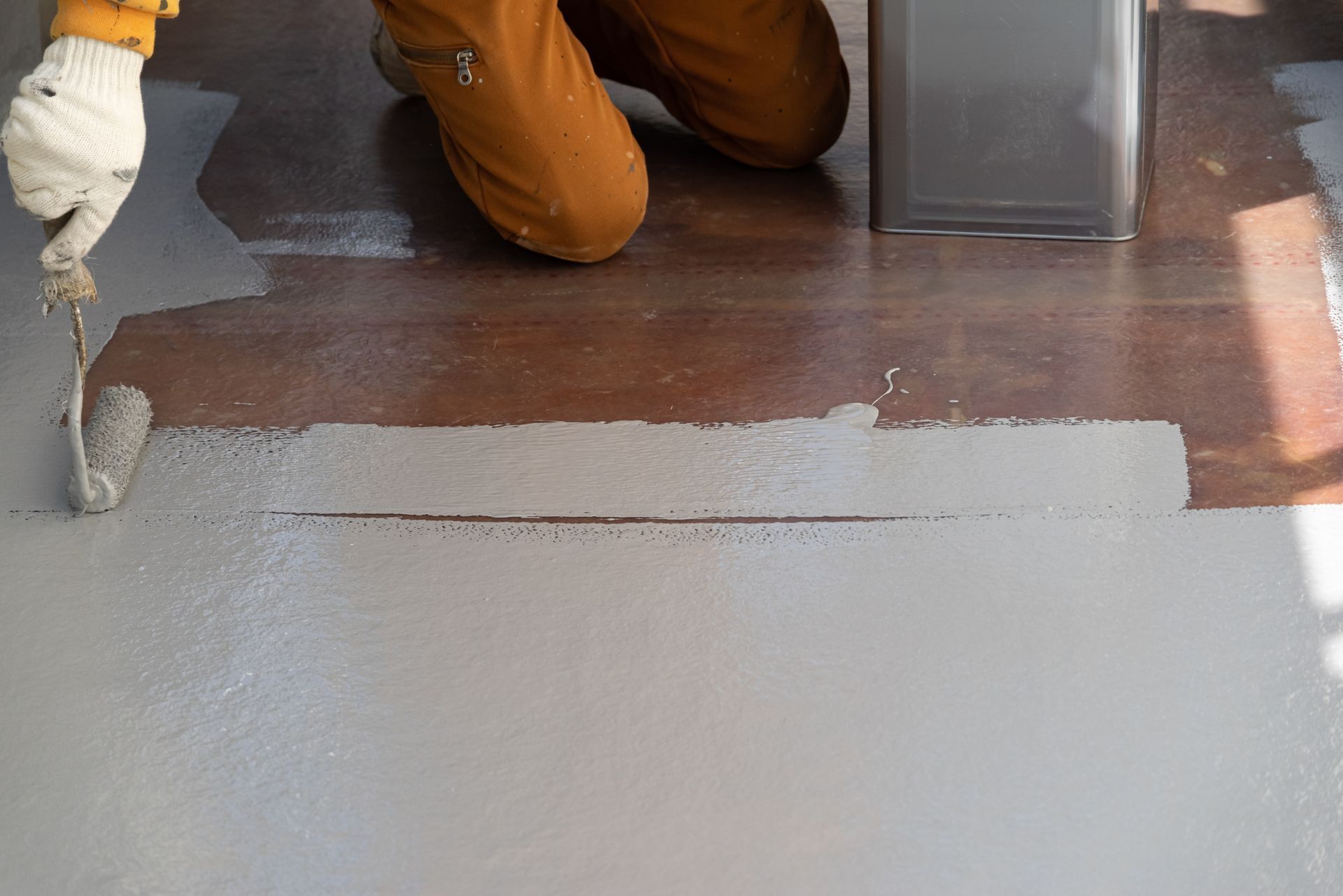 Person painting a wooden floor gray with a roller.