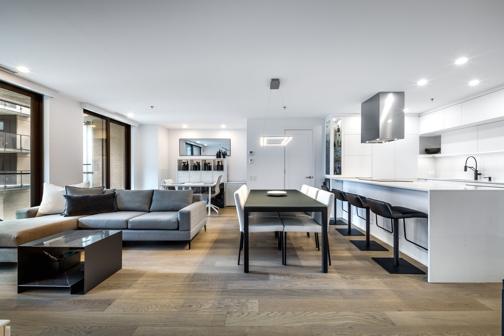 Modern open-plan living space with a kitchen, dining area, and living room. Neutral colors, natural light, and contemporary furniture.