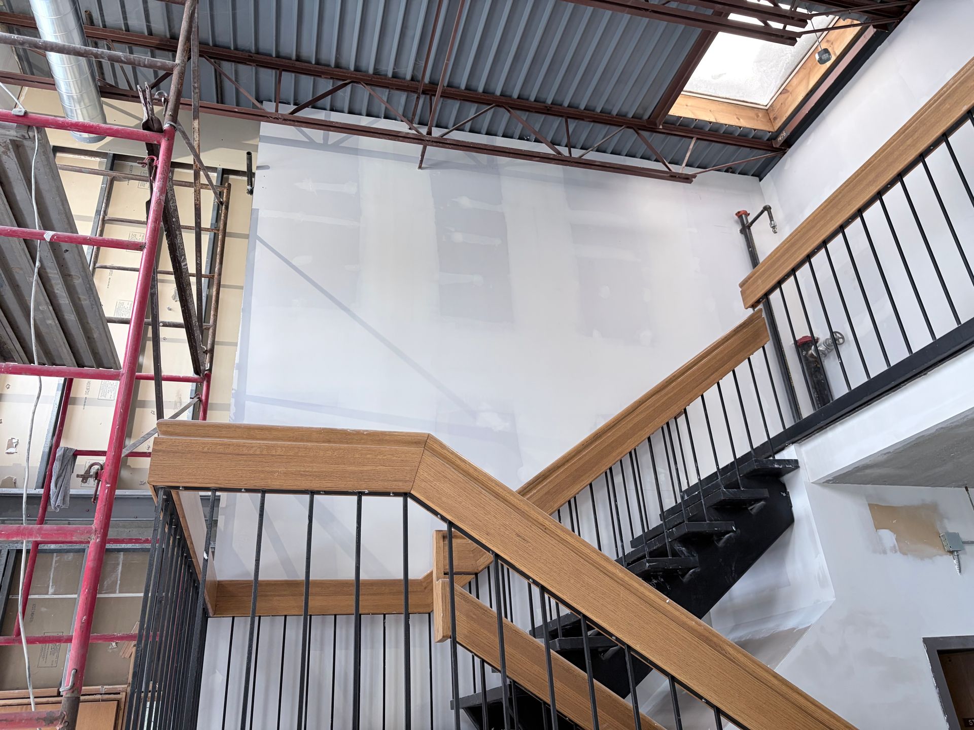 Interior construction view with staircase, exposed ceiling, scaffolding, and drywall.