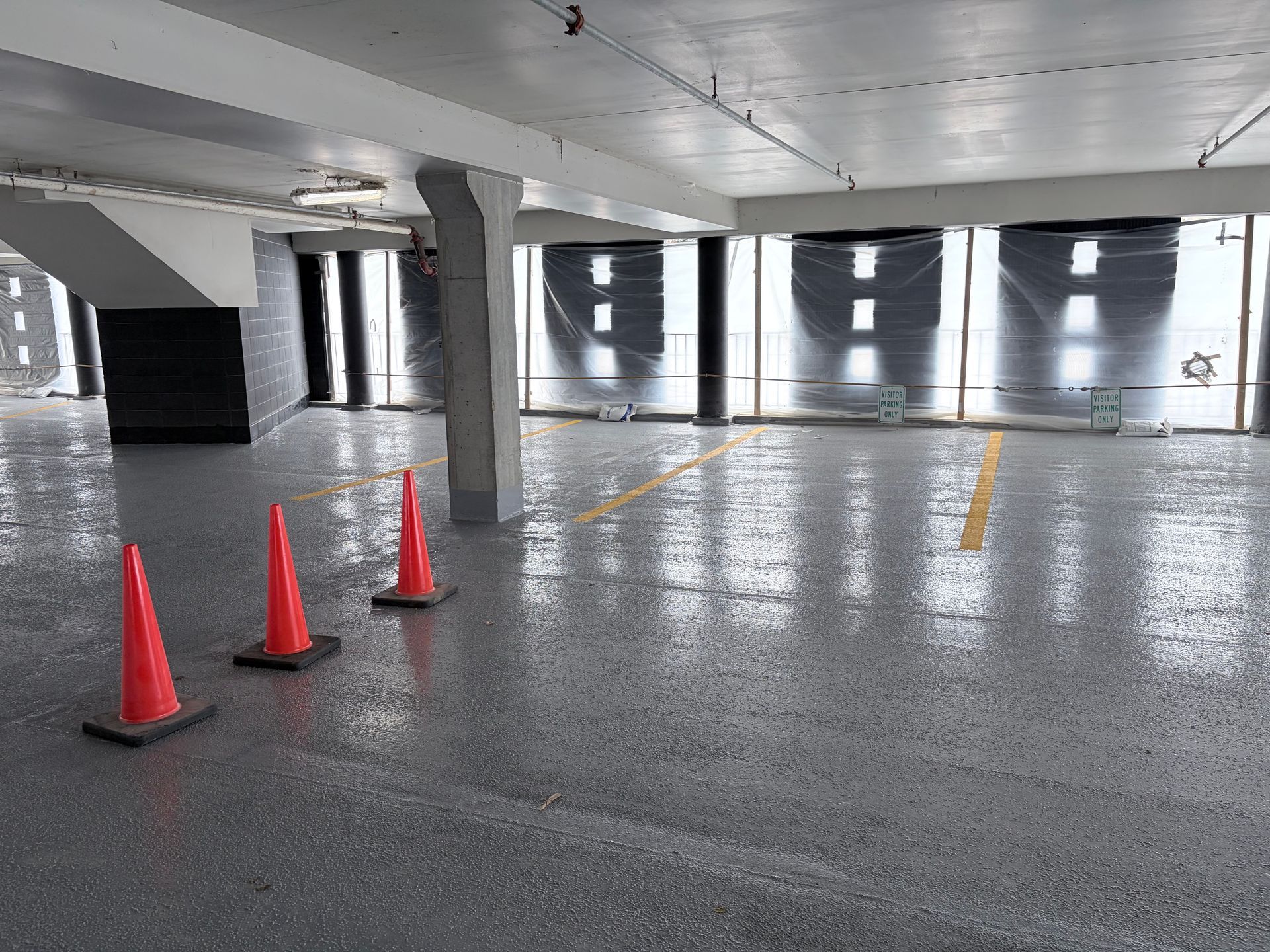 Indoor parking garage with three orange traffic cones on a reflective gray epoxy floor.