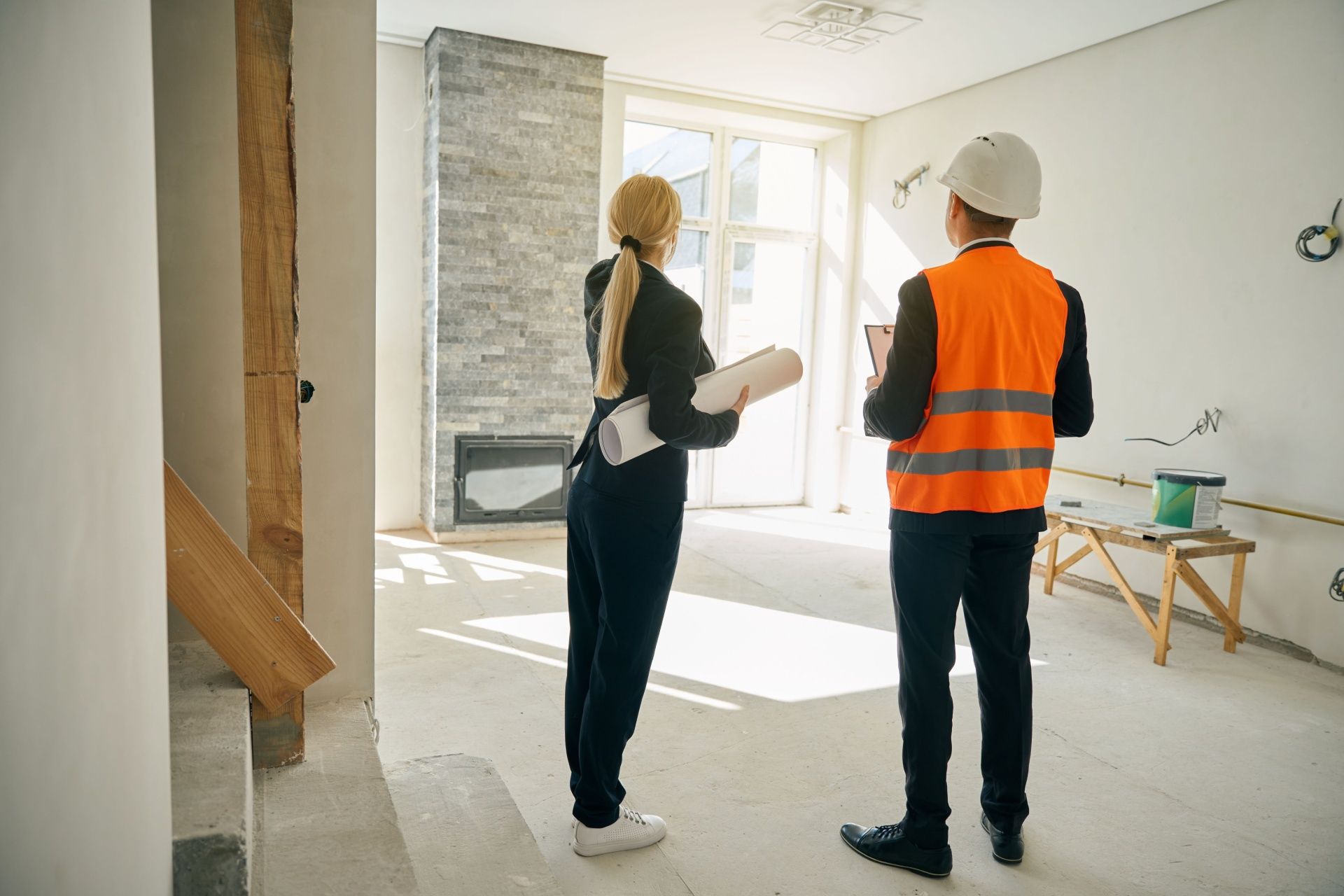 A man and a woman are standing in an empty room looking at a blueprint.