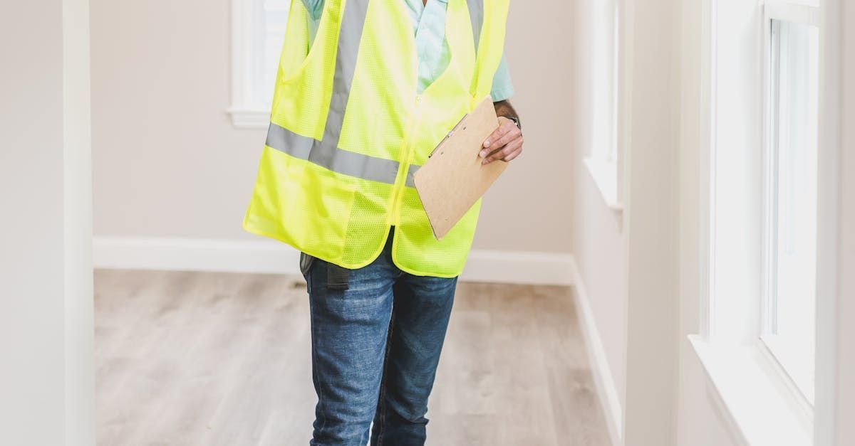 A man in a yellow vest is walking down a hallway holding a clipboard.