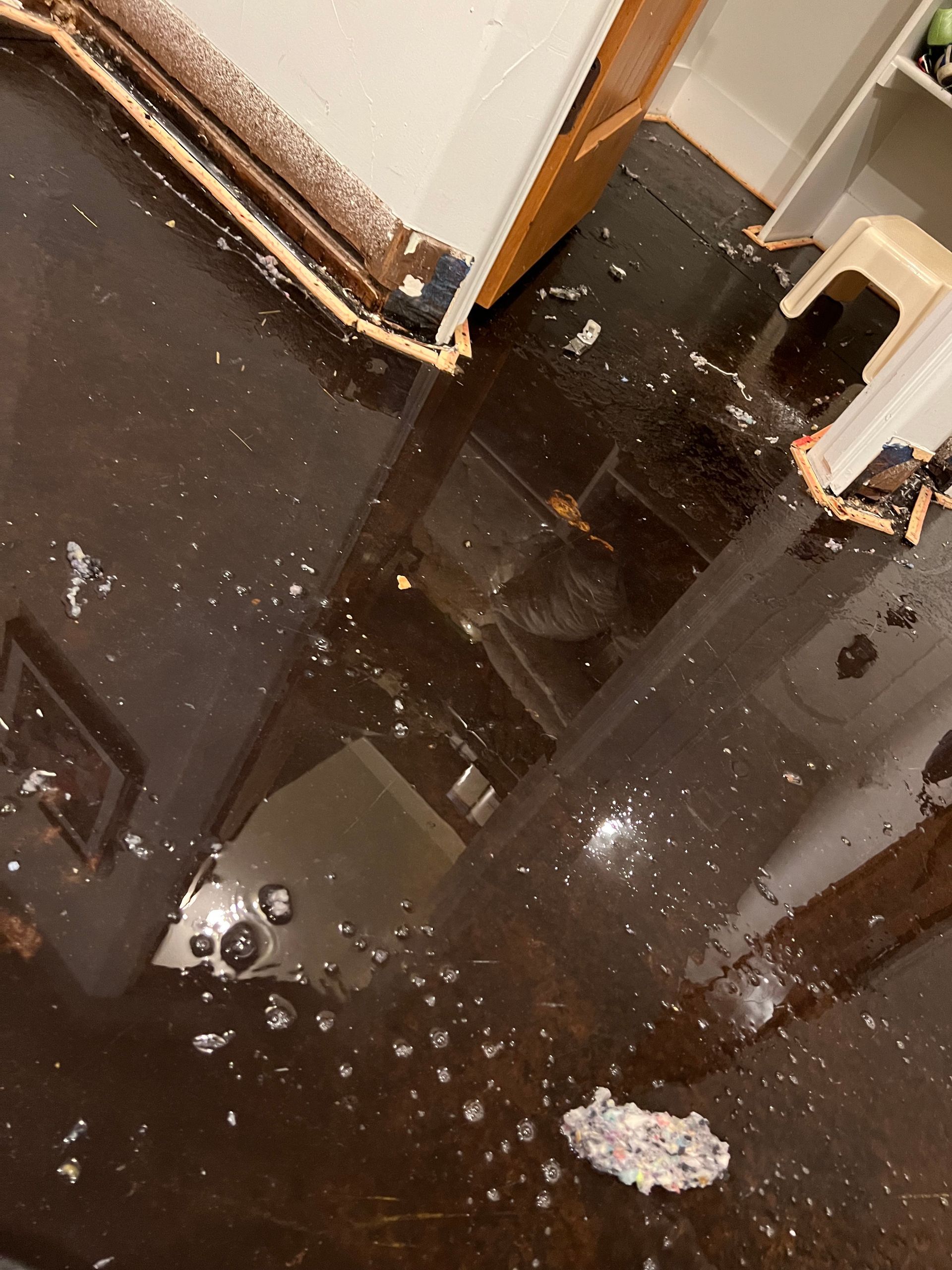 Wet tiled floor with scattered white debris near a doorway and cabinet.