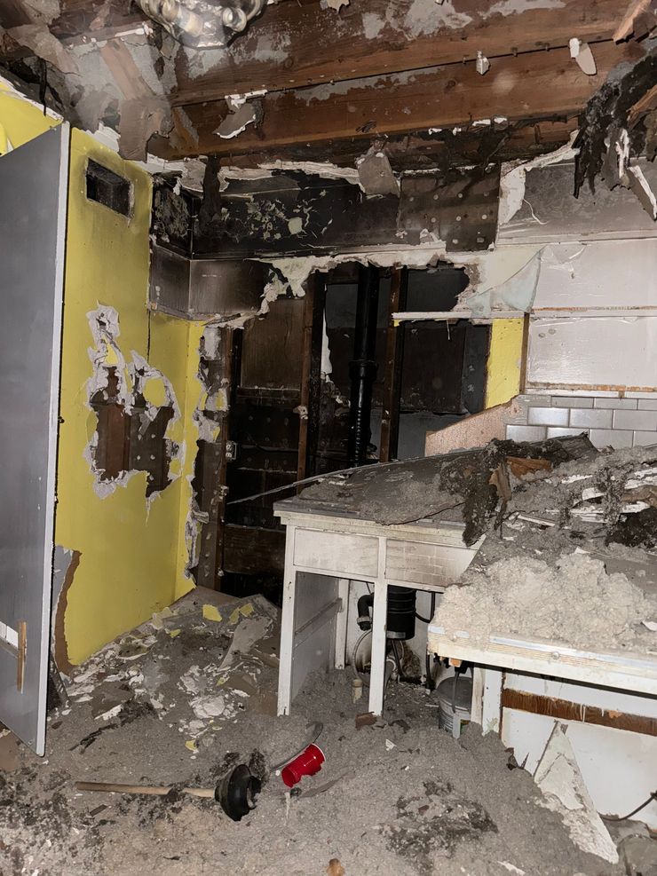Fire-damaged room with charred ceiling, debris, and a yellow cabinet near a table.