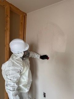 Person in protective suit applying paint to a wall in a room under renovation.