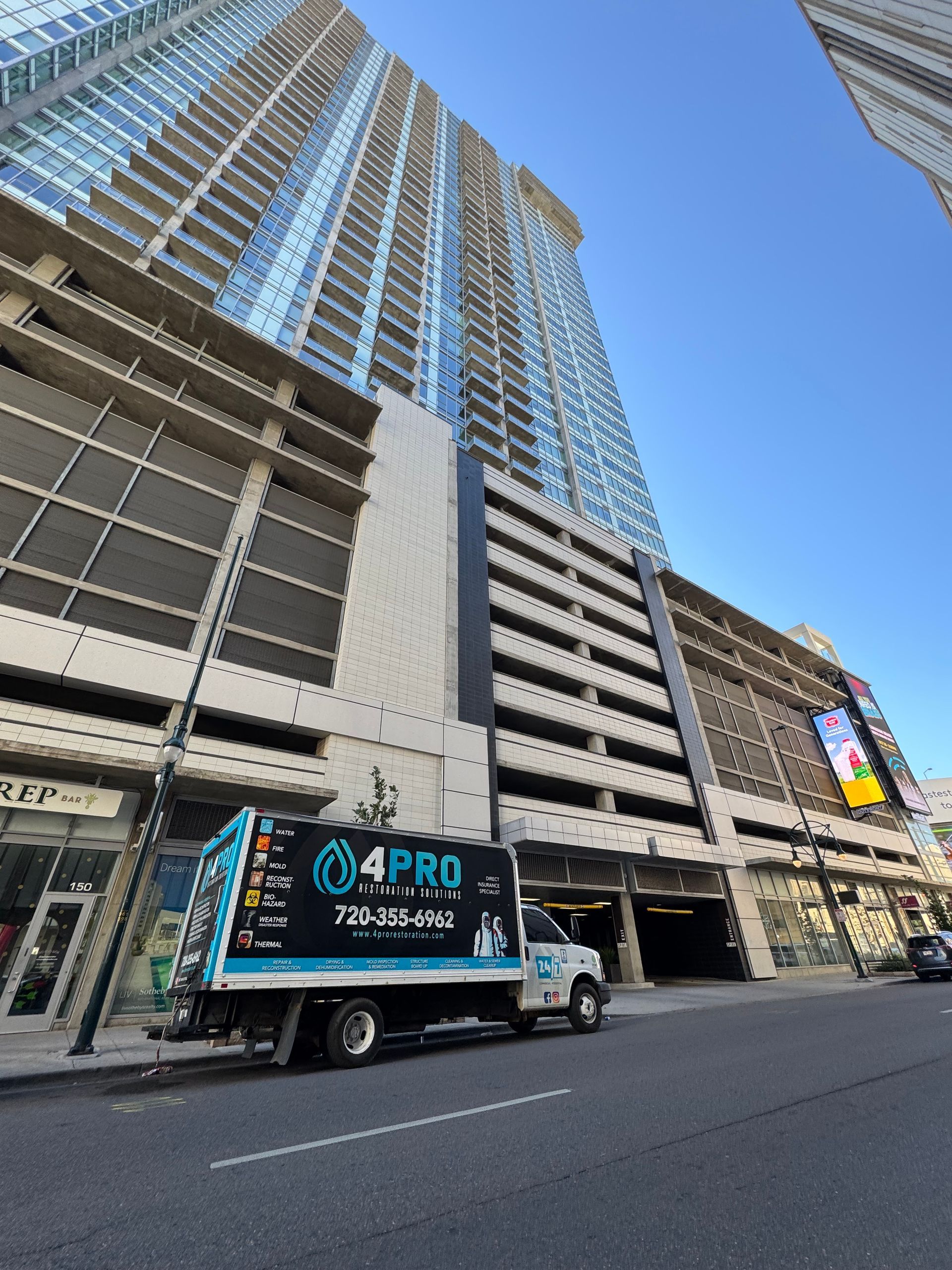 Tall city building with a 4PRO service truck parked on the street under a blue sky.