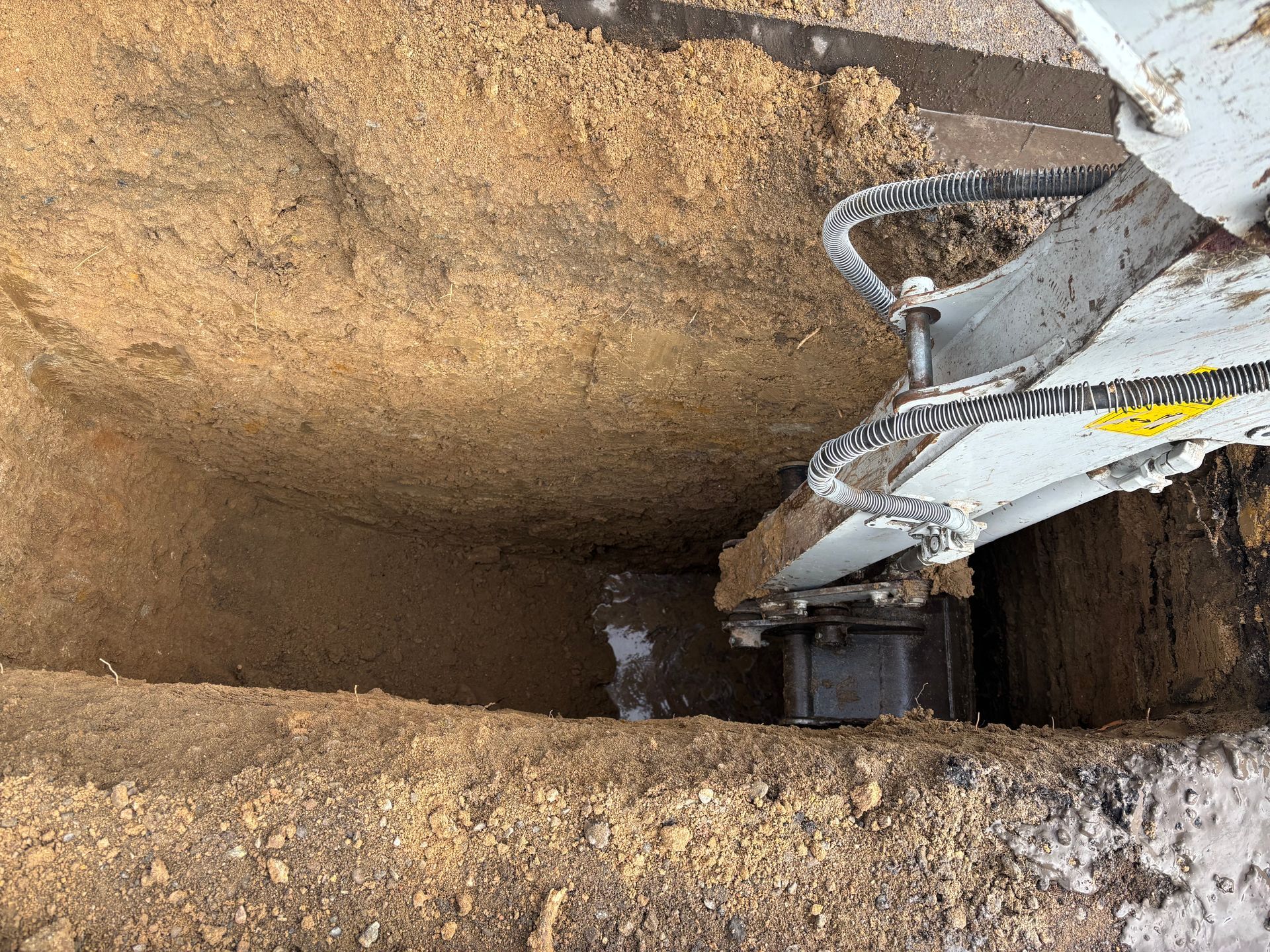 Top-down view of a deep dirt excavation with a white machine arm and gravel-lined edges