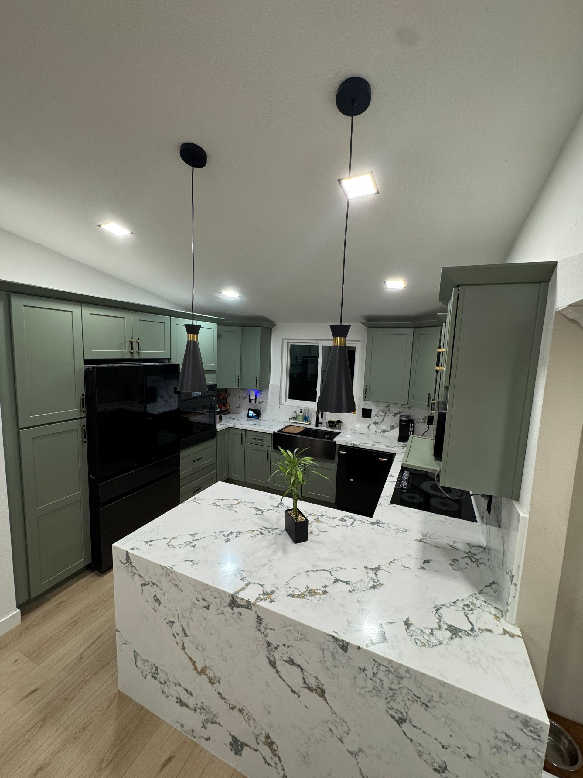 Modern kitchen with gray cabinetry, marble island, pendant lights, and black appliances