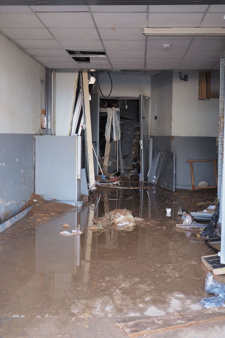 Flooded, damaged hallway with muddy water, broken ceiling tiles, and debris in a dim interior.