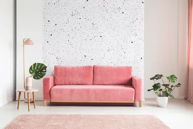Pink sofa in a bright minimalist living room with plants, side table, and speckled accent wall