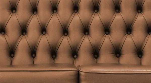 Nahaufnahme der Rückenlehne eines braunen, gesteppten Ledersofas mit rautenförmigem Knopfmuster.