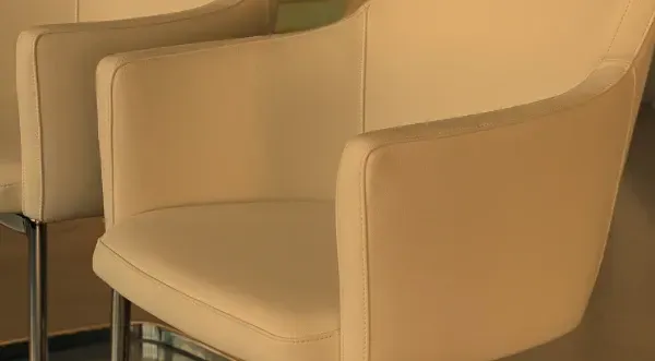 Zwei moderne, hellbeige Polstersessel mit schlanken Chrombeinen stehen nebeneinander in einem hellen Innenraum.