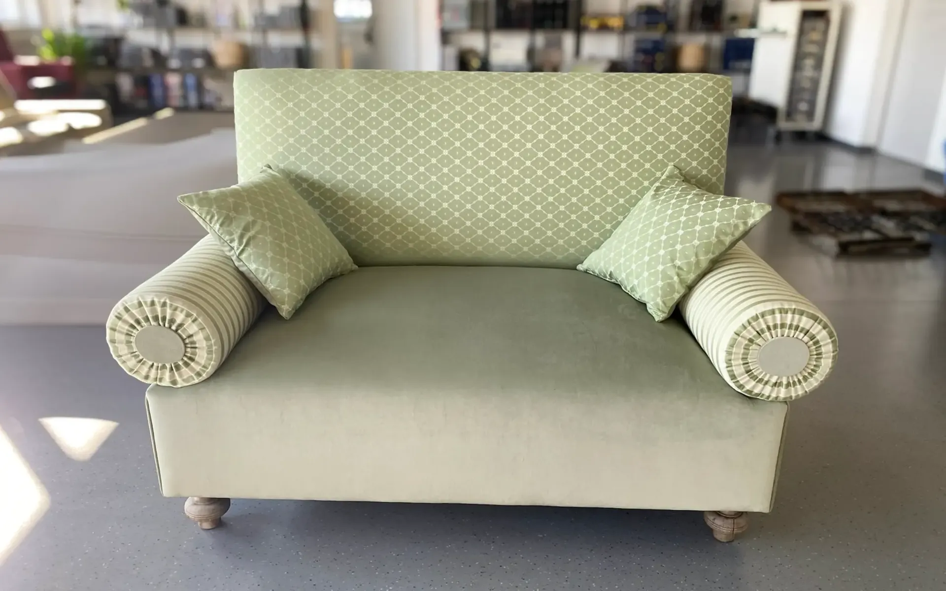 Ein hellgrünes, zweisitziges Sofa mit gemusterter Rückenlehne