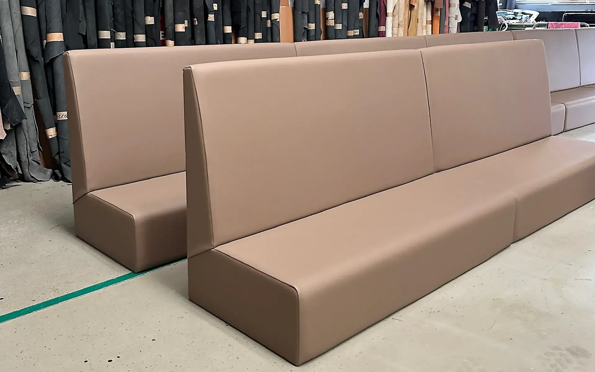 Zwei lange, hellbraune Restaurant-Sitzbänke mit klaren Linien stehen auf dem Werkstattboden.