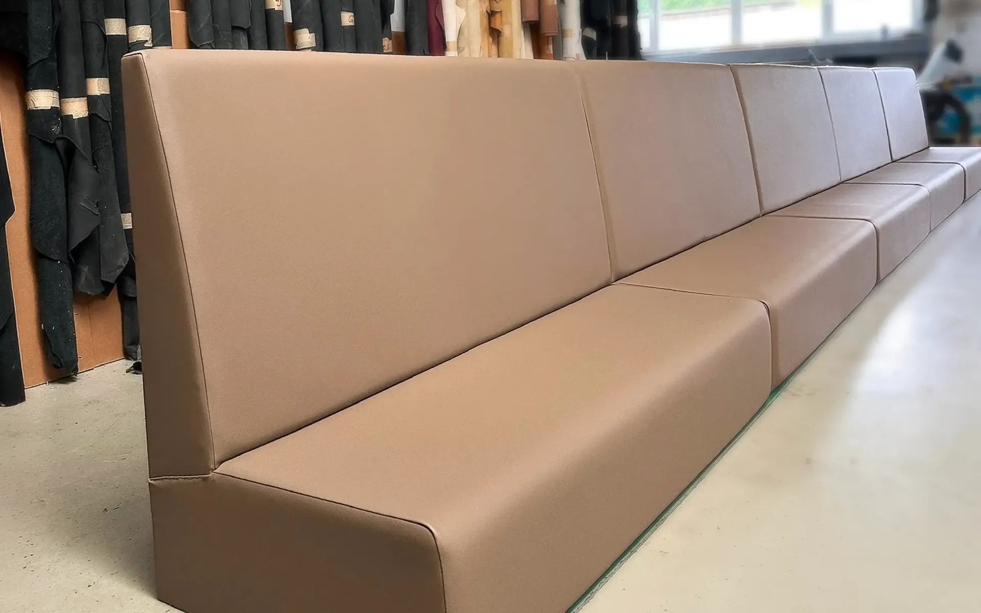 Ein langes, beigefarbenes Polstersofa mit klarem, modernem Design in einer Werkstattumgebung.