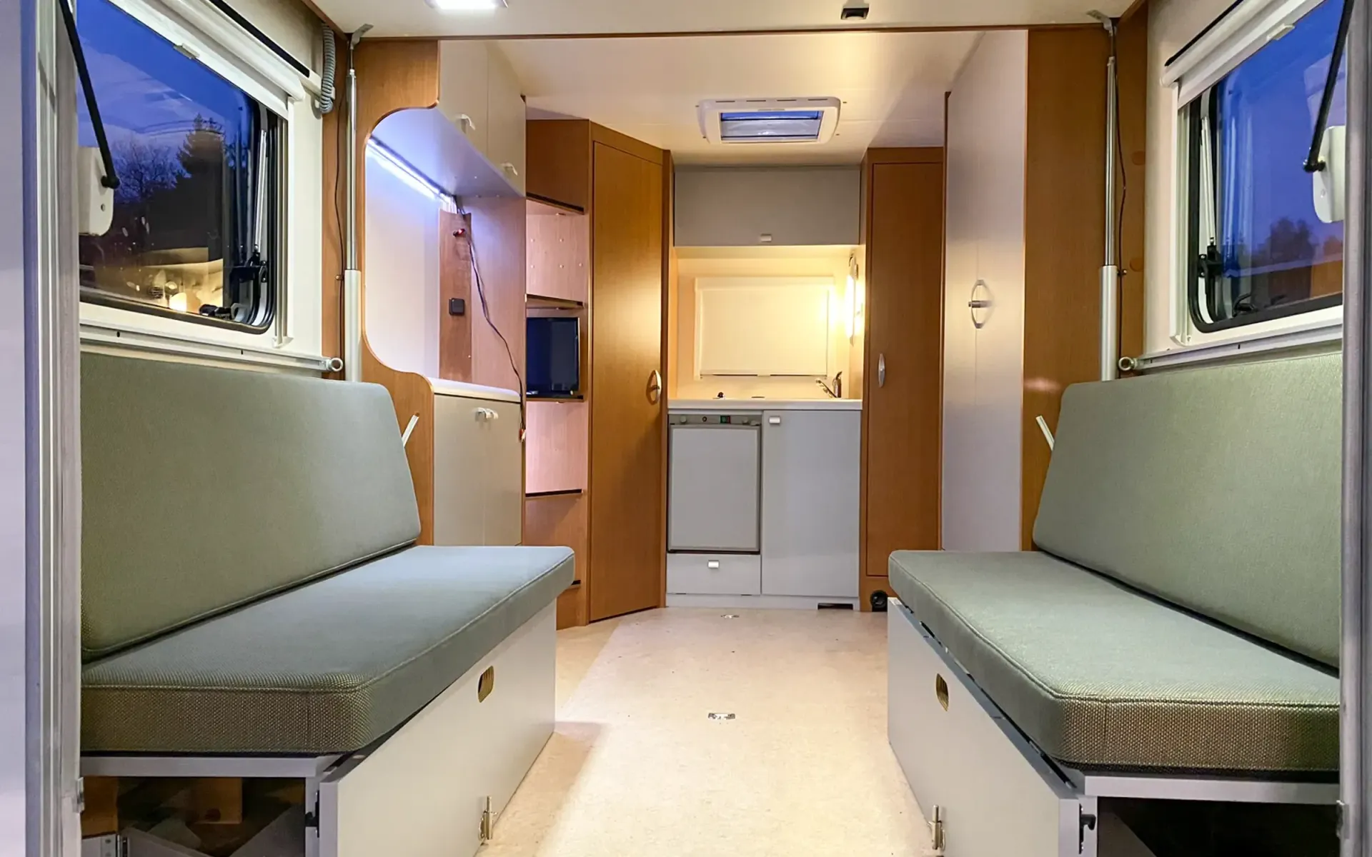 Innenansicht eines Wohnmobils mit zwei einander gegenüberliegenden grünen Sitzbänken, Schränken 