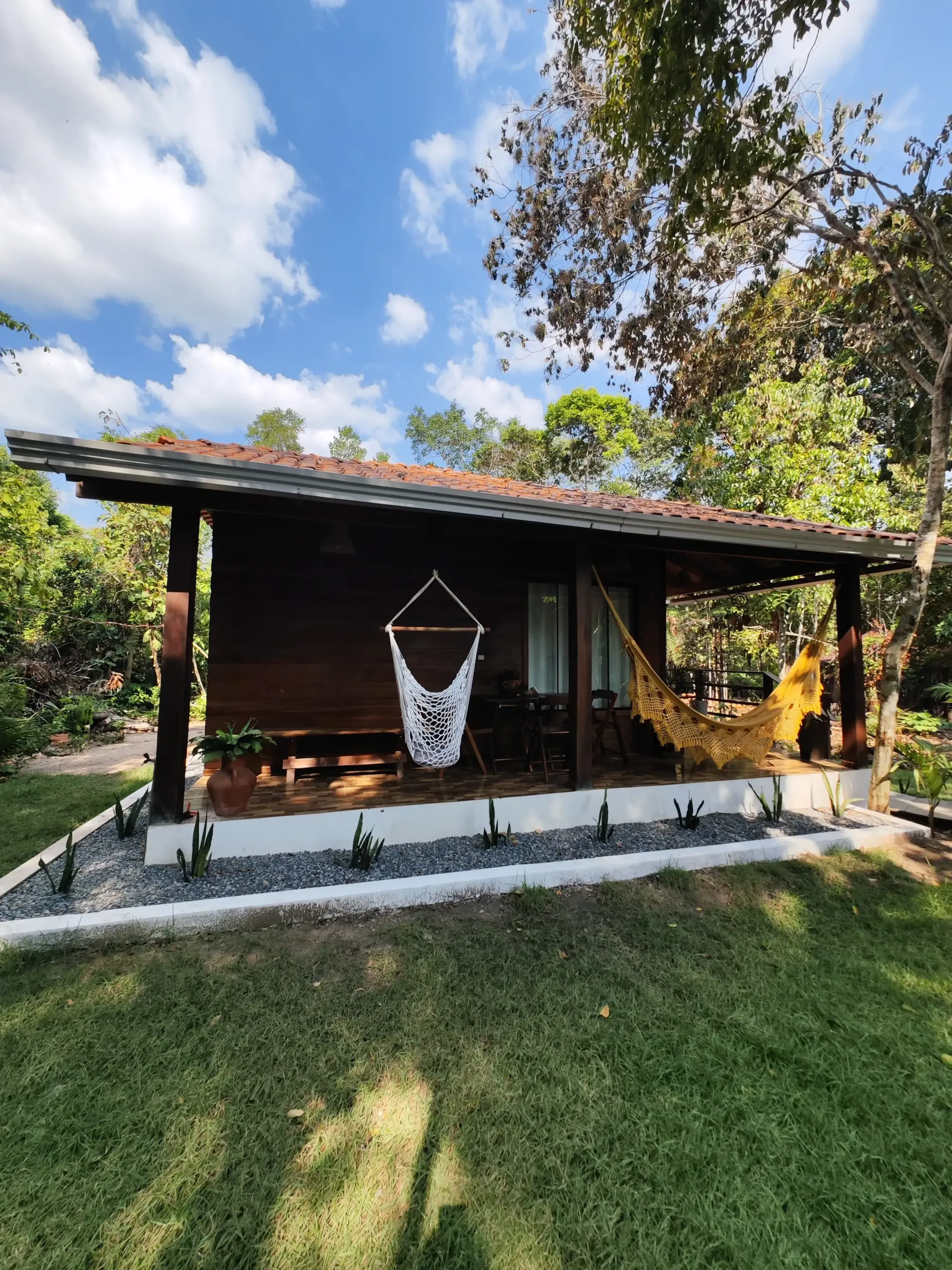 Uma pequena casa de madeira com uma rede na varanda. Pousada-Sumaúma