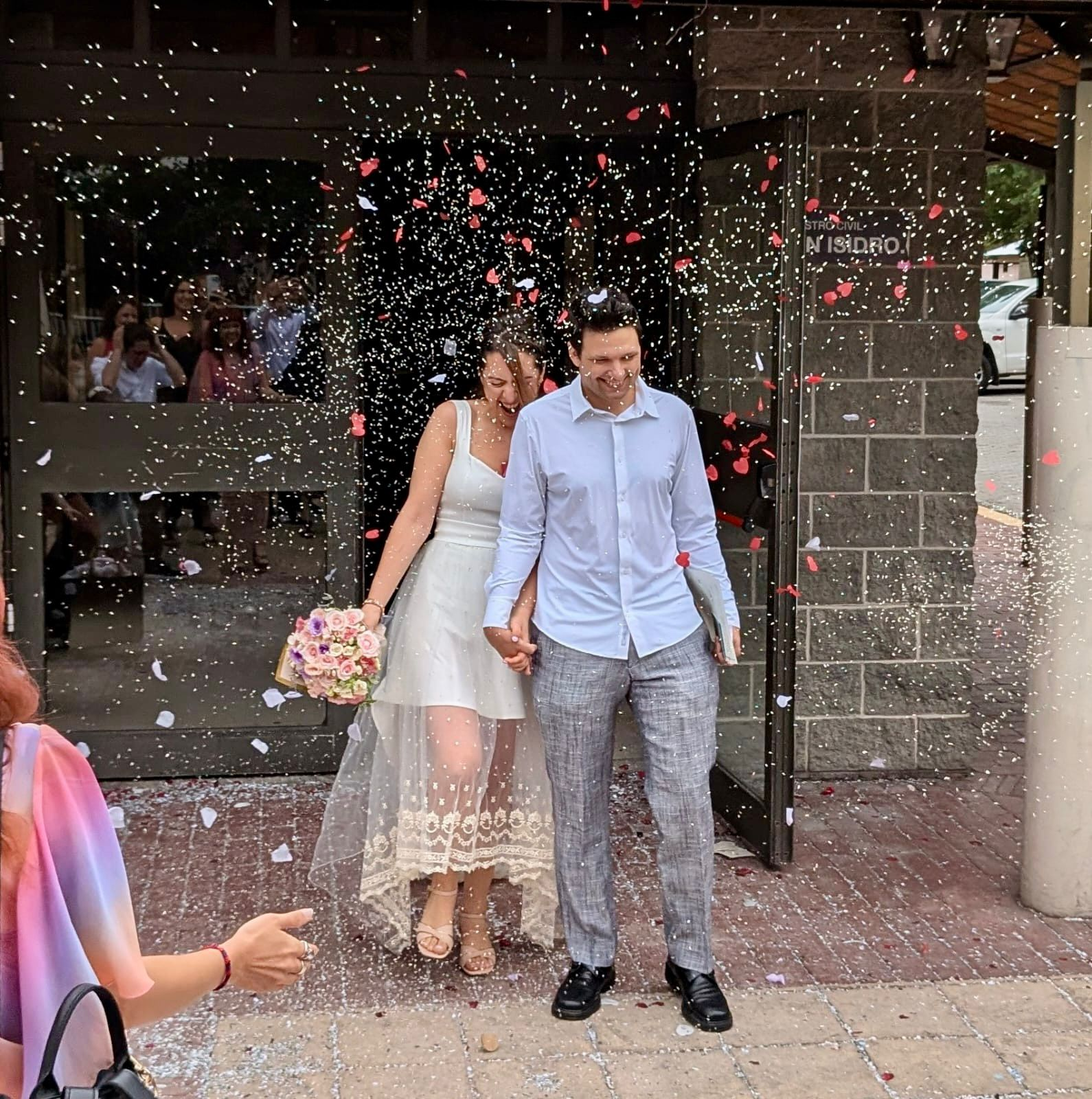Una pareja sale de un edificio de la mano mientras los invitados les lanzan confeti.