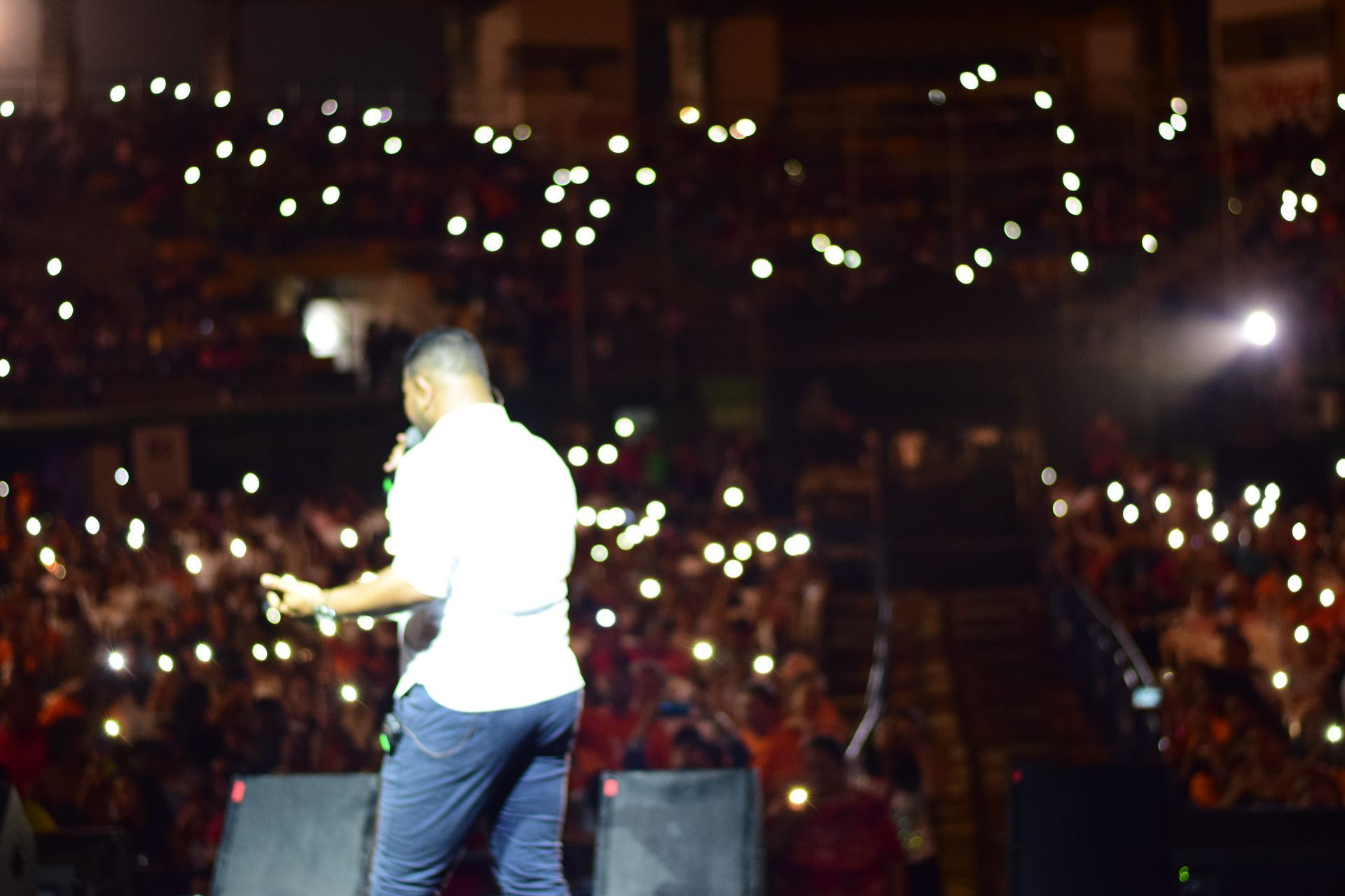 Una persona se encuentra de pie en un escenario oscuro frente a un público numeroso