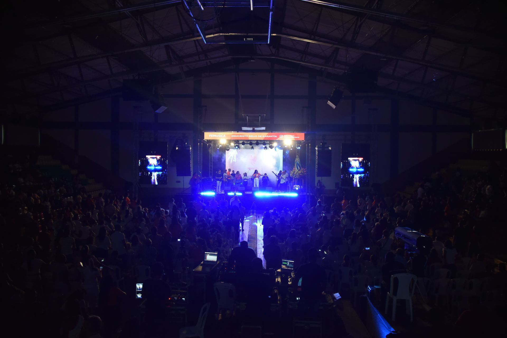 Una multitud observa una actuación en directo en un escenario con iluminación tenue, iluminado con luces azules brillantes